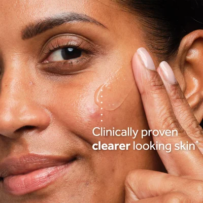 Close-up of a persons face applying a clear product to their cheek near the eye with the text Clinically proven clearer looking skin* overlaid.