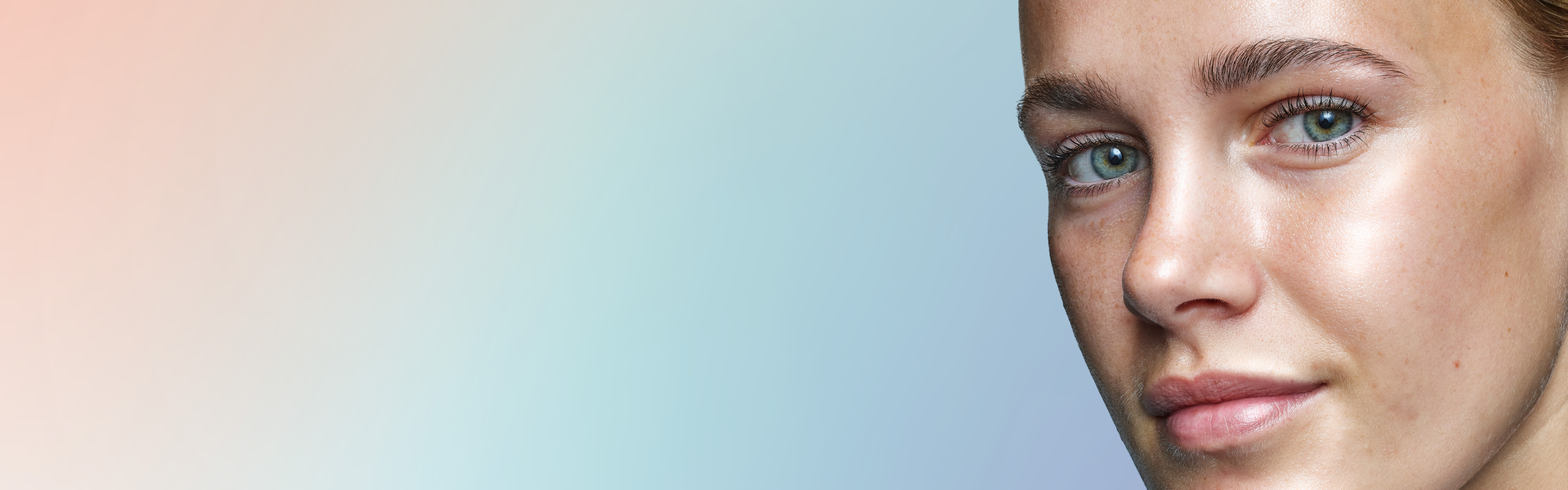 Ombre background with pastel shades of pink, white and blue. A close up shot of a female model is looking at the camera